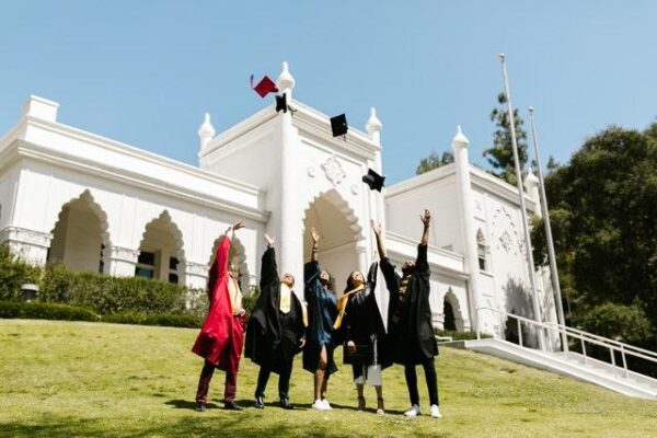 People wearing graduation gowns; tossing their graduation caps in the air